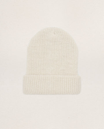 The Natural Alpaca Beanie in cream by THE GREAT. HOL 24 BIRKENSTOCK features ribbed knit from undyed yarn and a folded brim, shown on a plain light background.