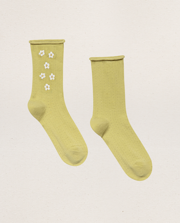 THE GREAT. SP25 POINTELLE SOCKS in Citron: one sock with delicate daisy embroidery and the other plain, both from The Pointelle Sock collection, displayed on a light textured background.