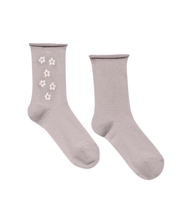 The Pointelle Sock by THE GREAT. SP25 features lavender ankle socks—one adorned with white daisy embroidery, the other plain.