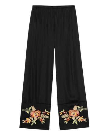 The Cuffed Pant by THE GREAT. PF25 is a black wide-leg pant with an elastic waistband and bouquet floral embroidery in orange, yellow, and green at the cuffs of each leg.