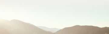 Sunrise over misty mountain range, with a soft gradient sky and warm sunlight illuminating the peaks.