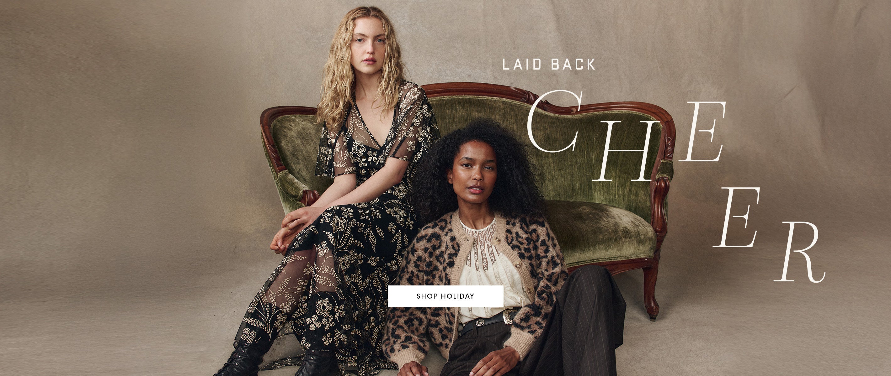 Two women sit on a vintage green velvet sofa, one wearing a black floral dress and the other in a leopard print cardigan, with "Laid Back Cheer" text in the background.