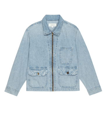 THE GREAT. PF25’s The Zip Front Chore Jacket in Dakota Wash features light blue denim, a collar, zip front, chest pocket, and two front flap pockets with buttons—classic workwear style shown on a plain background.