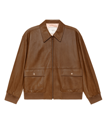 THE GREAT. F25 COLLECTORS' The Flight Jacket in Saddle Brown features heritage-inspired leather, a front zipper, two flap pockets with snaps, ribbed cuffs and hem, and a pointed collar. Shown on a plain white background.