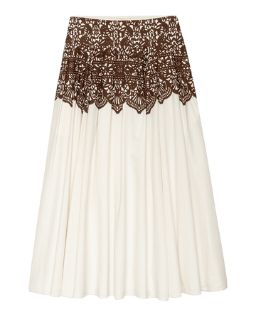 The Regency Skirt by THE GREAT. F25 D1 is a knee-length cream skirt with a brown western lace print overlay at the waist and upper section, pleated for a flared, elegant silhouette.
