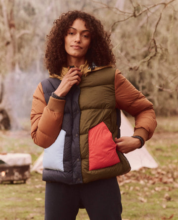 Wearing The Down Polar Puffer - Appalachian Colorblock by THE GREAT. FALL 24 TGO, a person stands outdoors amidst tents, fully embracing the essence of The Great Outdoors.
