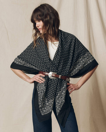 A person poses with hands on hips wearing The Big Bandana in Almost Black, secured with a brown belt over a white top and jeans. This stylish yet comfortable look features a 100% cotton scarf by THE GREAT. SP25 D2 brand.