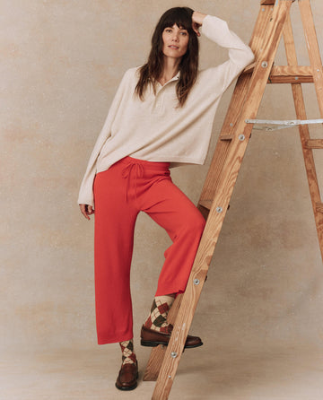 A person in a beige cashmere sweater and The Cashmere Lantern Pant in Ember by THE GREAT. HOL 24 CASHMERE stands next to a wooden ladder, wearing brown shoes with patterned socks.