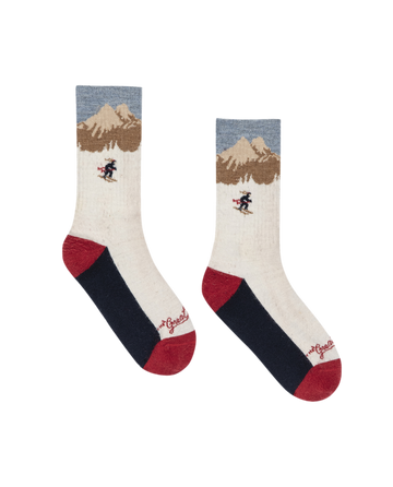 The Ridge Runner Sock – Cream Skiier by THE GREAT. F25 TGO is a merino wool sock with mountain and skier designs in cream, blue, red, and black, cushioned footbed for comfort, and "Goose" on the toes.