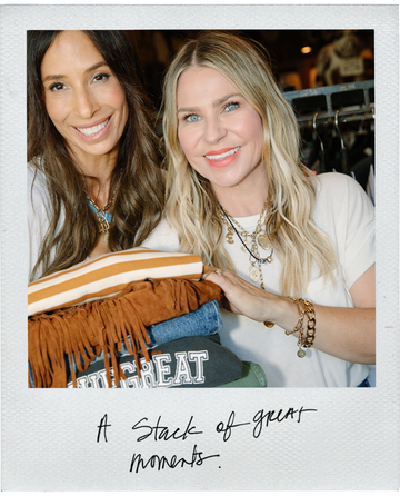 Two women smiling and holding a stack of clothes in a casual setting. Text reads, "A Stack of great moments.