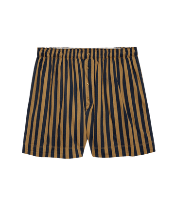The Sleep Boxer Short – Club Stripe by THE GREAT. F25 SLEEP features vertical navy and tan stripes, an elastic waistband, and button fly, shown on a black background.