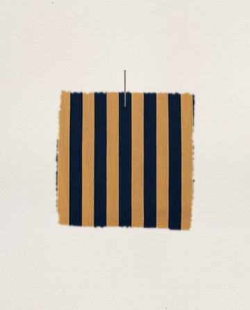 A rectangular swatch of THE GREAT. F25 SLEEP’s The Sleep Boxer Short – Club Stripe, featuring vertical navy blue and gold stripes, hangs centered against a plain off-white background.