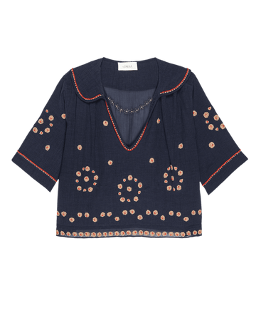 The Beaded Vintage Sailor Top by THE GREAT. SU25 is a navy blue sailor-style top with half sleeves, red embroidered edges, and beige and red circular floral patterns throughout the fabric.