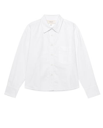 The Cropped Oxford Shirt in white by THE GREAT. F25 D1 features a collar, single chest pocket, and long sleeves, made from structured cotton oxford for tailored style. Displayed on a white background.