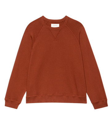 The Slouch Sweatshirt. Solid -- Brick by THE GREAT. F25 SEASONAL KNITS, a rust-colored vintage-inspired piece with long raglan sleeves, ribbed cuffs, and hem, handcrafted in Los Angeles, laid flat on a white background.