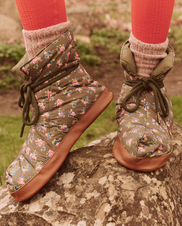 A person wearing The Down Quilted Puffer Slipper in Cypress Basin Floral from THE GREAT. FALL 24 TGO, paired with red socks, stands on a rock, showcasing their unique style and appreciation for technical clothing.