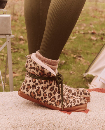 A person wearing leopard print boots and green tights stands outdoors, their look enhanced by The Down Quilted Puffer Slipper in Snow Leopard from THE GREAT. FALL 24 TGO collection.