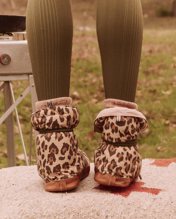 A person in The Down Quilted Puffer Slippers - Snow Leopard by THE GREAT. FALL 24 TGO and green ribbed leggings stands confidently on a mat outdoors, showcasing an ensemble that would pair perfectly with down puffer accessories for added style.