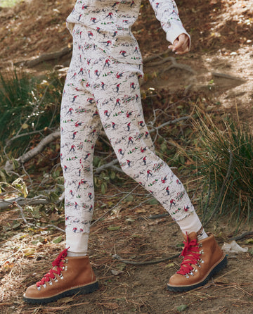 Wearing THE GREAT. F25 TGO The Union Long John -- Slopeside Print and brown hiking boots with red laces, this person walks outdoors on a dirt path covered with dry leaves and grass.