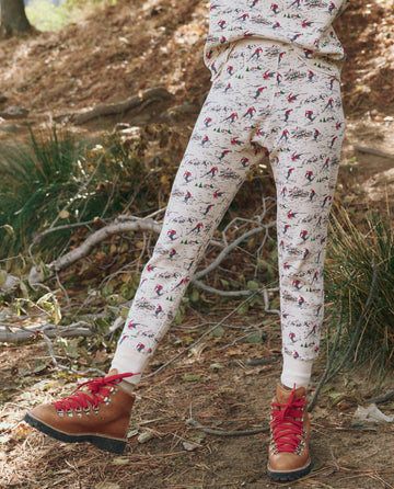 A person outdoors on a forest floor wears THE GREAT. F25 TGO's The Union Long John in Slopeside Print, paired with brown hiking boots with red laces and vintage menswear thermals for cozy layering.