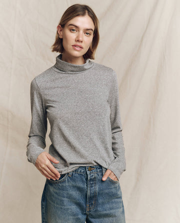 A person showcases a fashion-forward look in The Turtleneck. -- Heather Grey by THE GREAT. HOL 24 TURTLENECKS, paired with jeans, standing against a neutral backdrop while confidently gazing at the camera.