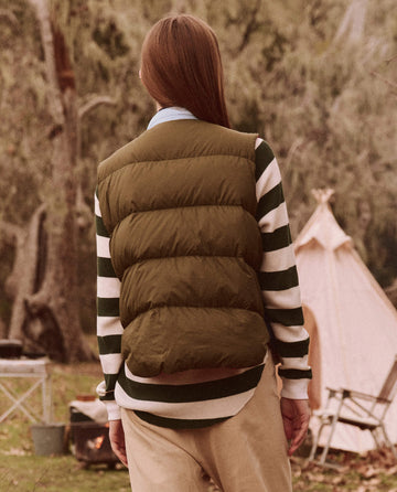 A person is outdoors near a tent and camping chairs, wearing The Down Polar Vest in Appalachian Colorblock by THE GREAT. FALL 24 TGO, which features responsibly sourced down, ready with their adventure accessories.