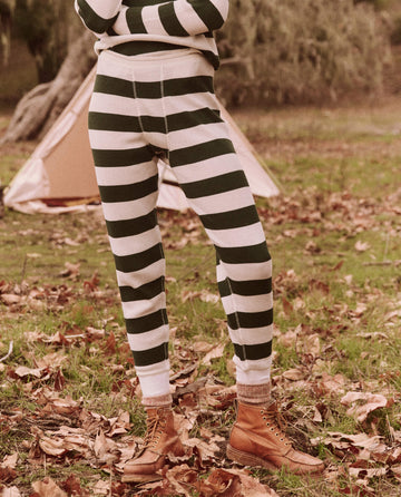 Dressed for an everyday adventure, a person stands amidst fallen leaves in front of a tent, wearing The Union Long John in Mountain View Stripe and brown boots, offering both comfort and durability as part of THE GREAT. FALL 24 TGO collection.