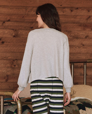 A person wearing The Sleep Cut Off Sweatshirt in Light Heather Grey from THE GREAT. HOL 24 SLEEP and striped pants stands with their back to the camera in a room with wooden walls, creating the perfect cold-weather set.