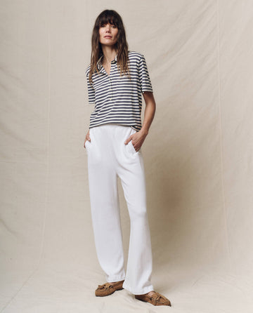 A person stands against a plain background, hands in pockets, confidently wearing a striped polo shirt paired with THE GREAT. SP25 POLO LOUNGE's The Victory Sweatpant in True White.
