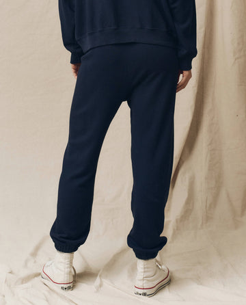 A person is shown from the back, wearing The Stadium Sweatpant in True Navy by THE GREAT. FALL 23 KNITS, paired with a matching sweatshirt and white high-top sneakers. The backdrop is a plain, light-colored fabric.