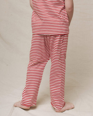 A child wearing The Little Jersey Crop by THE GREAT. in Sun Cherry Stripe stands barefoot on a light fabric surface.