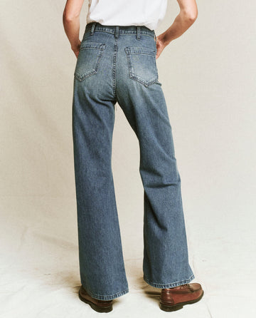 Back view of a person wearing The Dock Jean in Marina Wash and brown shoes, standing against a plain background.