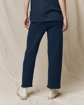 A person wearing The Wide Leg Cropped Sweatpant in True Navy by THE GREAT. FALL 23 KNITS and white sneakers stands with their back to the camera against a beige backdrop.