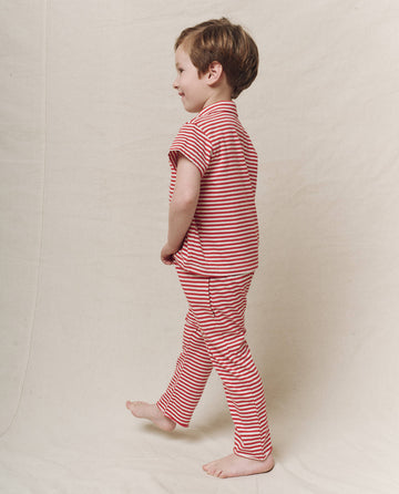 A child in The Little Jersey Crop by THE GREAT. SP25 POLO LOUNGE LITTLE, Sun Cherry Stripe design, stands sideways against a plain background.