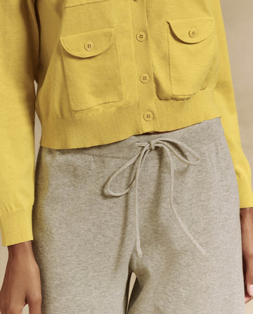 Person wearing a yellow button-up sweater and THE GREAT. SP25 HIGH TWIST YARN Heather Grey Lantern Pant, shown from shoulders to mid-thigh, adding an elegant twist to modern fashion.