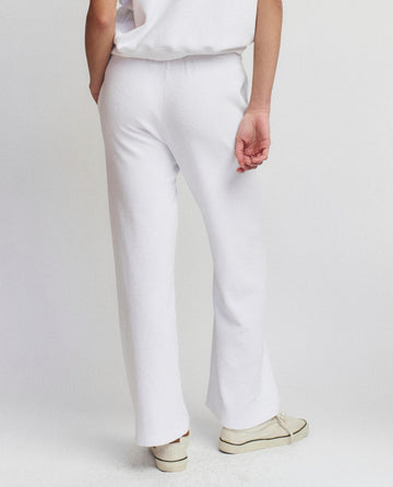 A person stands against a plain background in THE GREAT. SU25 MICRO TERRY The Micro Terry Victory Sweatpant in True White, paired with a matching top and shoes—their back turned for an effortless style statement.