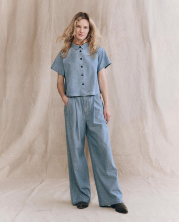 A person stands against a neutral backdrop wearing THE GREAT. PF25’s Sawyer Pant in Boiler Wash, hands in pockets, highlighting this stylish and modern wide-leg design.