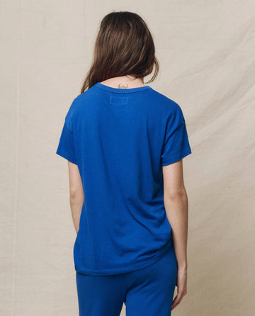 Clad in THE GREAT. SP25 KNITS' The Boxy Crew, Solid -- Bright Cobalt and pants, an individual in casual wear faces away from the camera against a plain backdrop.