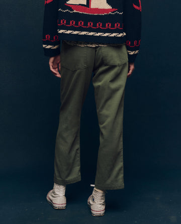 The individual is clad in a patterned sweater and The Vintage Army Pant by THE GREAT. SP25 COLLECTORS, complemented by white high-top sneakers, as they stand against a dark backdrop, captured from behind.