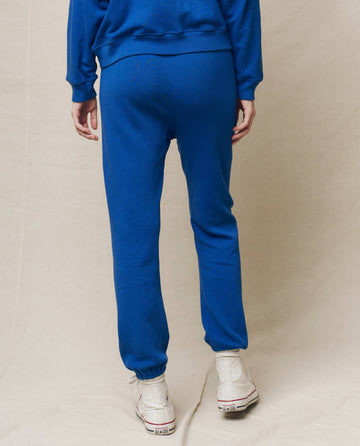 A person wearing The Stadium Sweatpant in Bright Cobalt from THE GREAT. SP25 KNITS and white sneakers stands on a light background, facing away.