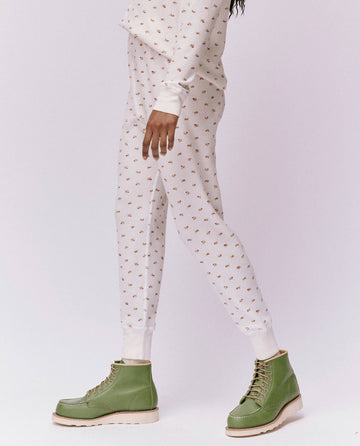 A person in The Waffle Long John from THE GREAT. HOL 24 ROSEBUD CAPSULE, featuring a White Mini Heirloom Rose pattern, and green boots stands against a plain background.