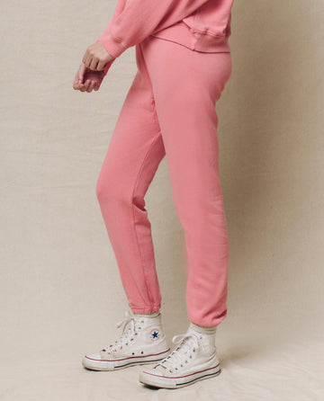 A person in The Stadium Sweatpant by THE GREAT. SP25 KNITS, paired with a pink sweater and white sneakers with a star logo, stands before a neutral backdrop. This confetti-colored activewear offers comfort for casual outings and relaxed days alike.