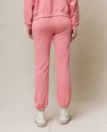 A person in a pink tracksuit and white sneakers displays The Stadium Sweatpant in Solid -- Confetti from THE GREAT. SP25 KNITS, standing back to the camera against a plain background.