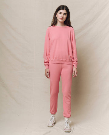 In front of a beige backdrop, a person wears THE GREAT. SP25 KNITS The College Sweatshirt in Solid -- Confetti with matching pants and chic white sneakers.