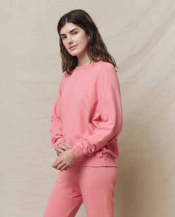 A person in The College Sweatshirt in Confetti color by THE GREAT. SP25 KNITS and matching pants stands against a light beige background, gazing at the camera with clasped hands.