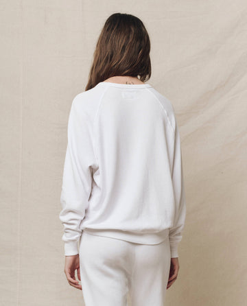 A person with long brown hair is wearing The College Sweatshirt in True White by THE GREAT. HOL 24 KNITS, along with matching pants, and is facing away against a plain beige background.