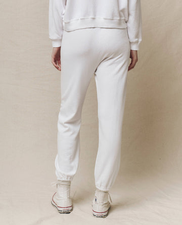 A person wearing THE GREAT. HOL 24 KNITS's The Stadium Sweatpant in True White, featuring an elasticated waist, stands with their back to the camera. The vintage athletic vibe is completed by sleek white high-top sneakers and a matching white sweatshirt.