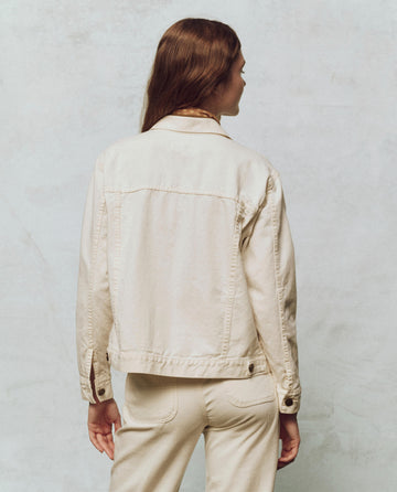 Someone with long hair is wearing The Workwear Jean Jacket in Natural Hemp from THE GREAT. PS25 and pants, viewed from the back.