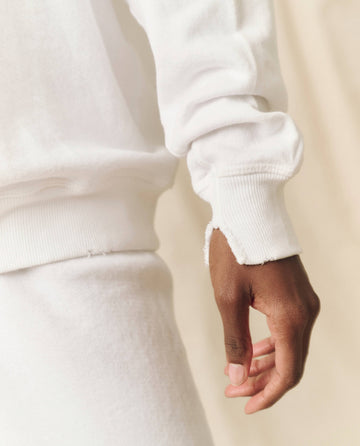 Close-up of a person wearing The College Sweatshirt in True White from THE GREAT. FALL 24 KNITS collection, focusing on their arm, hand, and the texture of the fabric.