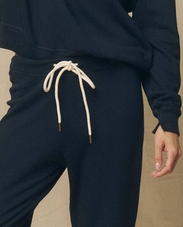 A person wearing The Cropped Sweatpant in True Navy from THE GREAT. FALL 23 KNITS, complete with a light drawstring and a matching dark sweatshirt, standing with their hand relaxed at their side.